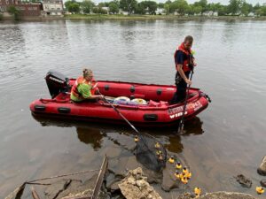 Two people in red rubber boat on river using nets to catch yellow rubber ducks