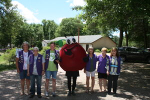 Wisconsin Rapids Lionesses standing next to Cranberry Guy mascot with trees in background
